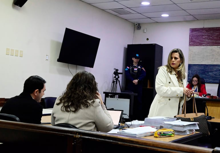 Kattya Mabel González Villanueva con cabello rizado usa un ordenador portátil, mientras un hombre de saco negro habla en una sala formal.