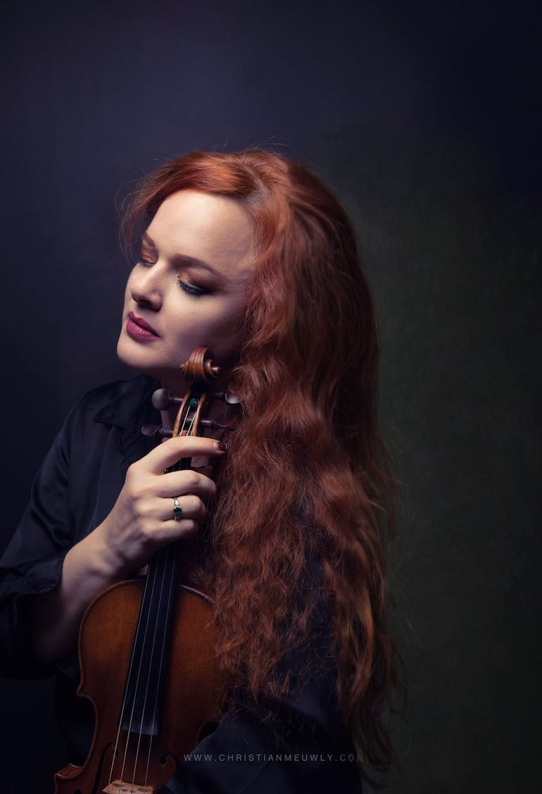 Rachel Kolly en traje formal, sosteniendo su violín, centrada en la actuación con expresión tranquila.