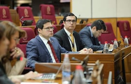 Óscar Orué en traje azul y corbata roja, rodeado de senadores en un ambiente formal de discusión.