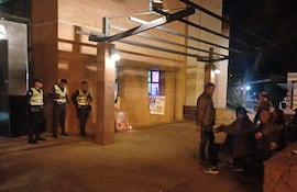 Cuatro agentes de policía, uniformados, observan mientras un hombre dialoga con otros en un ambiente nocturno iluminado.
