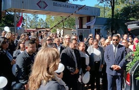 Grupo de personas vestidas de negro reunidas frente al Ministerio Público, con un ataúd decorado y expresión de tristeza.