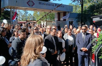 Grupo de personas vestidas de negro reunidas frente al Ministerio Público, con un ataúd decorado y expresión de tristeza.