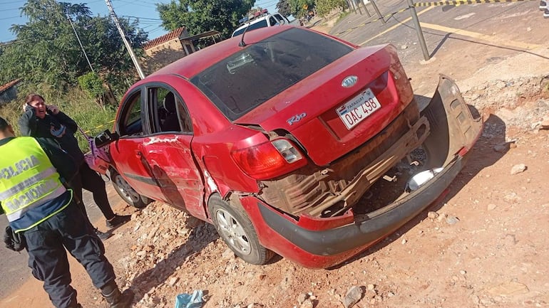 Automóvil dañado en la carretera, junto a un policía agachado y una mujer angustiada hablando por teléfono.
