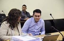 Hernán Rivas habla con cabello rizado, mientras un hombre de camisa de cuadros observa pensativo en un tribunal.