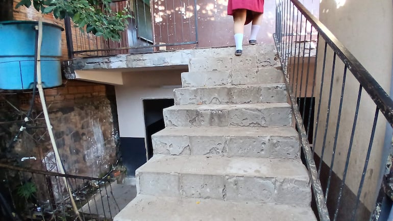 Estudiante en uniforme escolar de falda roja y medias blancas subiendo una escalera de cemento en un ambiente sencillo.