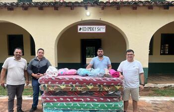 Diego Gómez sonríe sosteniendo algo, rodeado de hombres que ayudan con colchones y mantas en un ambiente exterior colorido.