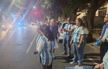 Seis personas con camisetas de la selección argentina celebran en la calle, rodeadas de banderas y un ambiente festivo nocturno.