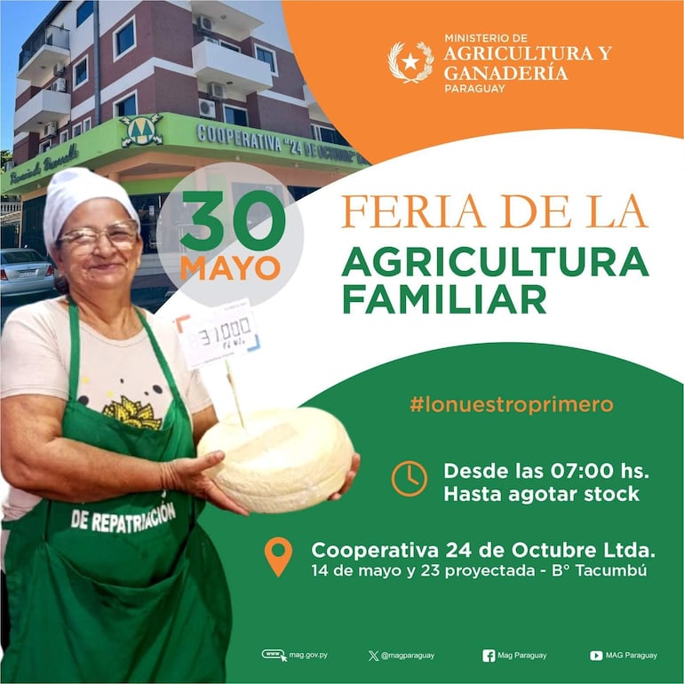 Mujer mayor sonriente con blusa clara y delantal verde, sostiene un queso frente a la cooperativa 24 de Octubre en ambiente de feria.