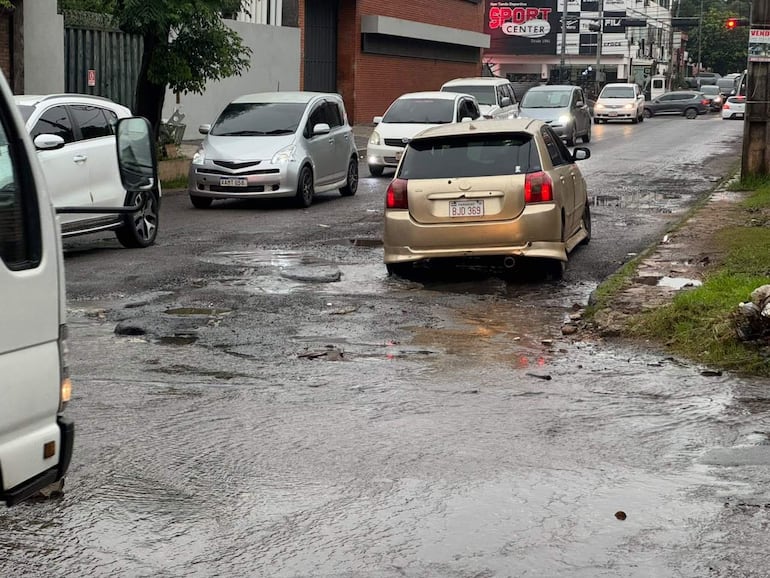 Automóviles estacionados y en movimiento en una calle inundada, sin personas visibles, ambiente urbano.