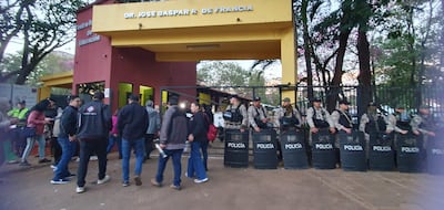 Multitud de adultos en el Centro Regional de Educación, algunos conversando mientras policías resguardan el acceso con escudos.