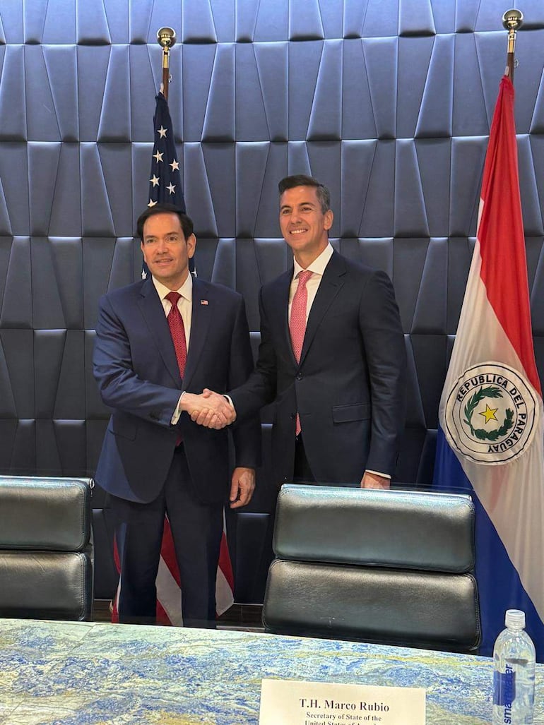 Rubio con traje oscuro y corbata roja estrecha la mano a Peña, también con traje oscuro y corbata rosa, bajo banderas de EE.UU. y Paraguay.