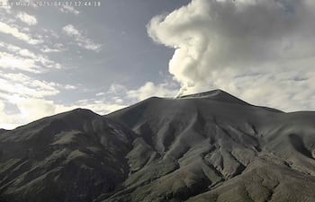 Volcán Puracé en erupción, mostrando columna de humo en un entorno natural montañoso con cielo parcialmente nublado.