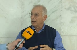 Gustavo Masi, con cabello canoso y camisa azul, habla mientras sostiene un micrófono en un interior formal.