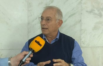 Gustavo Masi, con cabello canoso y camisa azul, habla mientras sostiene un micrófono en un interior formal.