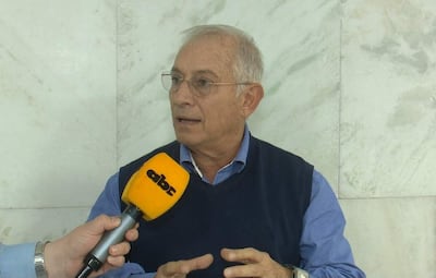 Gustavo Masi, con cabello canoso y camisa azul, habla mientras sostiene un micrófono en un interior formal.