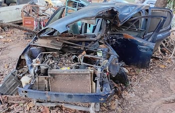 Un vehículo dañado, con el motor expuesto, rodeado de hojas secas y otros automóviles en mal estado.