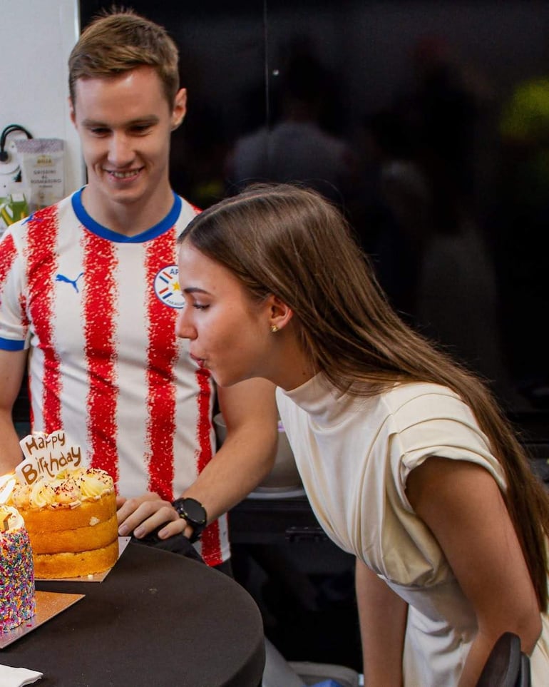 Willa Grissin Rosmaring sopla las velas de su pastel, rodeada de Joshua Duerksen, sonriente, en un ambiente festivo.