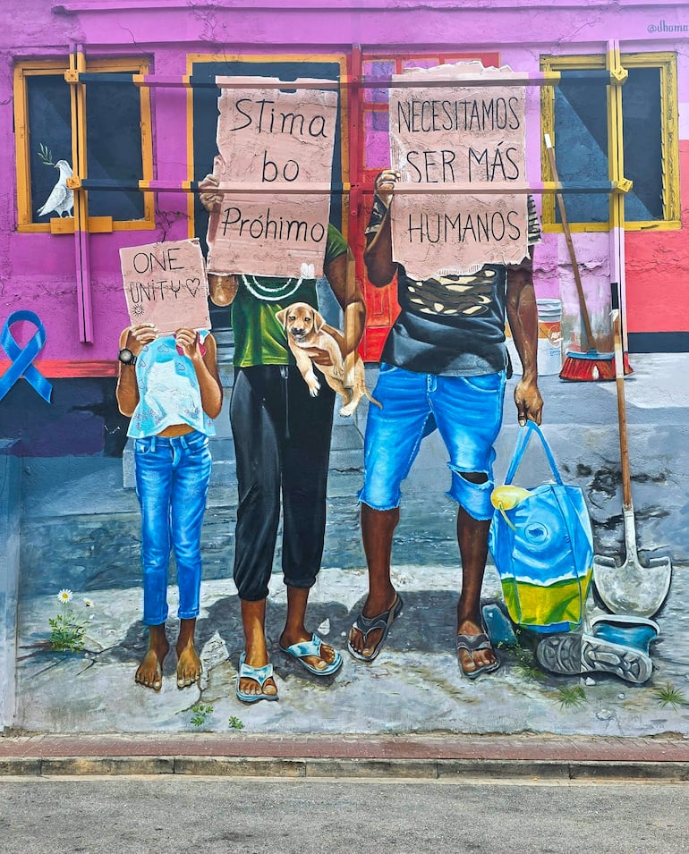 Niño y dos adultos frente a un mural colorido, sosteniendo carteles con mensajes sobre unidad. Ambiente comunitario vibrante.