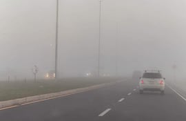 Dos coches, uno blanco y otro negro, avanzan por la carretera en medio de una densa neblina en la Costanera.