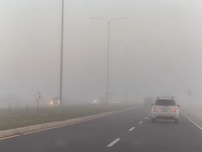 Dos coches, uno blanco y otro negro, avanzan por la carretera en medio de una densa neblina en la Costanera.