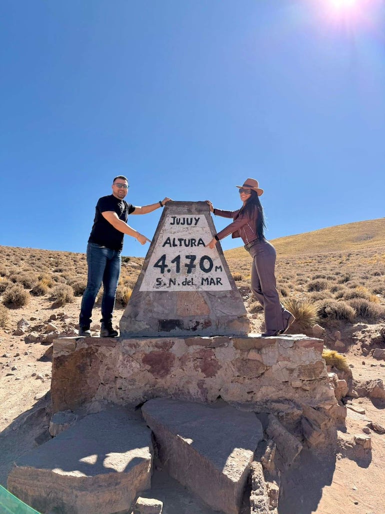 Gloria Vera con camiseta negra y gafas, y Julio Cáceres en chaqueta marrón, señalando un monolito en un entorno montañoso.