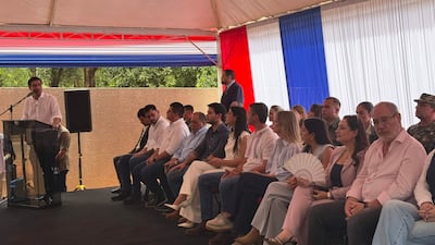 Santiago Peña en traje blanco habla al micrófono, rodeado de asistentes atentos bajo una carpa con los colores de la bandera paraguaya.