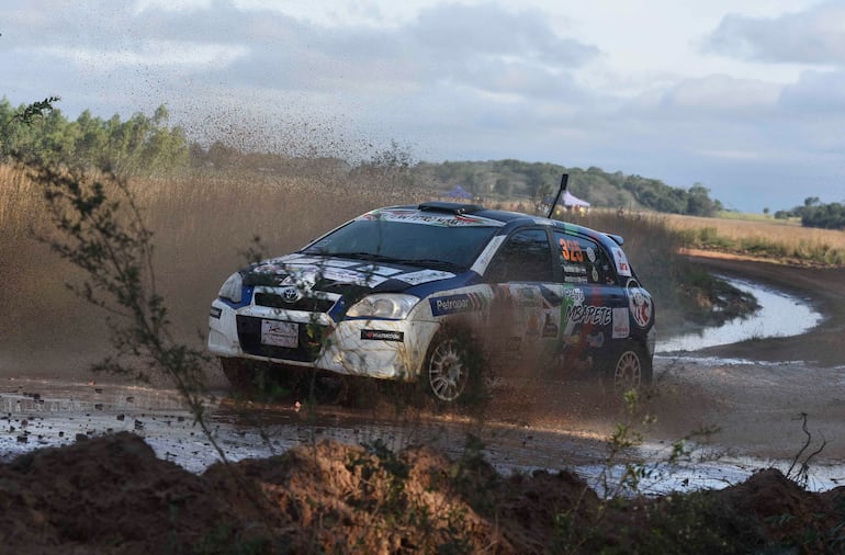 Toyota rally en plena carrera sobre pista de tierra, levantando polvo y agua en un ambiente natural.