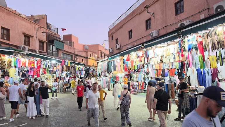 Personas con sombreros y ropa colorida socializan entre puestos de venta en un bullicioso mercado de Marrakech.
