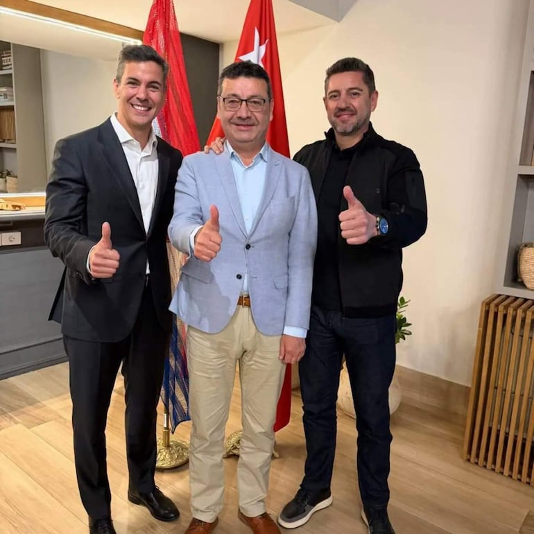 Santiago Peña, Pedro Alliana y Freddy D'ecclesiis sonríen con pulgar hacia arriba en un interior moderno con detalles de madera.