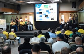 Cinco participantes en el evento, tres en camisetas amarillas aplauden, mientras uno habla y dos escuchan atentamente en un auditorio.