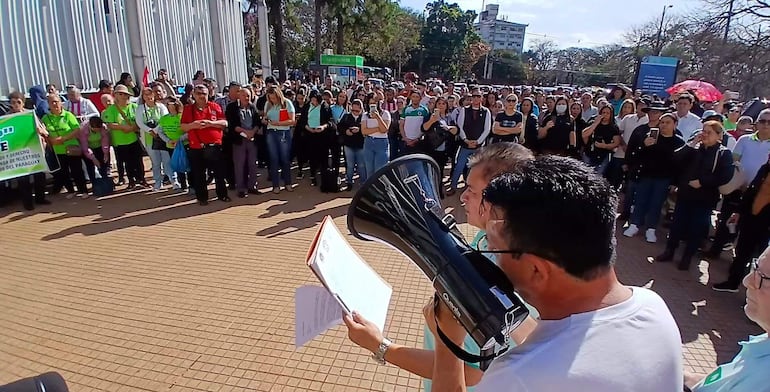 Hombres oradores con megáfono y documento, mientras la multitud de camisetas verdes escucha atentamente en un ambiente participativo.