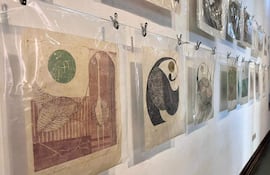 Obras de Lotte Schulz en galería, colgadas en la pared, rodeadas de plásticos y ganchos metálicos en ambiente luminoso.