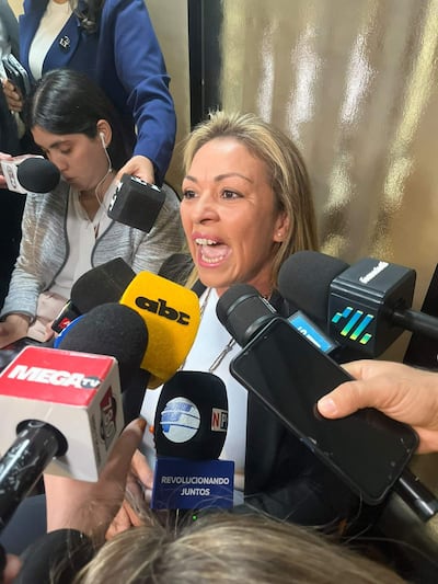 Fátima Delgado en conferencia, con cabello largo y claro, hablando con entusiasmo y rodeada de micrófonos de medios.