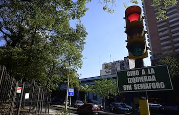 Semáforo en rojo y verde en intersección despejada, rodeada de árboles y edificios en un día soleado.