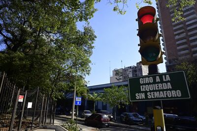 Semáforo en rojo y verde en intersección despejada, rodeada de árboles y edificios en un día soleado.