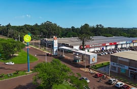 Gran cartel publicitario junto a carretera en Minga Guazú, con vehículos estacionados y árboles alrededor.