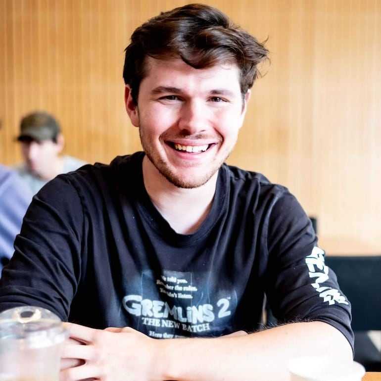 Robert Capron sonríe con dimples, luciendo un atuendo casual en un evento de Comic Con, rodeado de fanáticos emocionados.