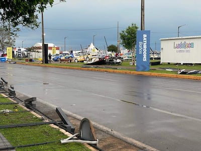 Ambiente urbano mojado y nublado con señales de baños, sin personas visibles, vehículos de competición en el fondo.