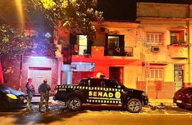 Dos agentes de la SENAD, en uniformes rojos, de pie junto a un vehículo rotulado, en una calle del barrio La Encarnación de Asunción, donde se detuvo a una sospechosa de microtráfico.