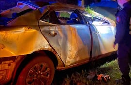 Rescatista en traje oscuro evalúa coche dañado y cubierto de barro, rodeado de luces de emergencia en un entorno oscuro.