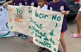 Niños con camisetas moradas sostienen un gran cartel que dice 'Yo 177', al aire libre en un ambiente urbano.
