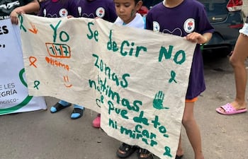 Niños con camisetas moradas sostienen un gran cartel que dice 'Yo 177', al aire libre en un ambiente urbano.