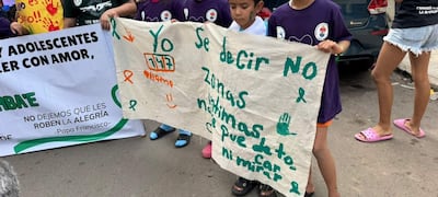 Niños con camisetas moradas sostienen un gran cartel que dice 'Yo 177', al aire libre en un ambiente urbano.