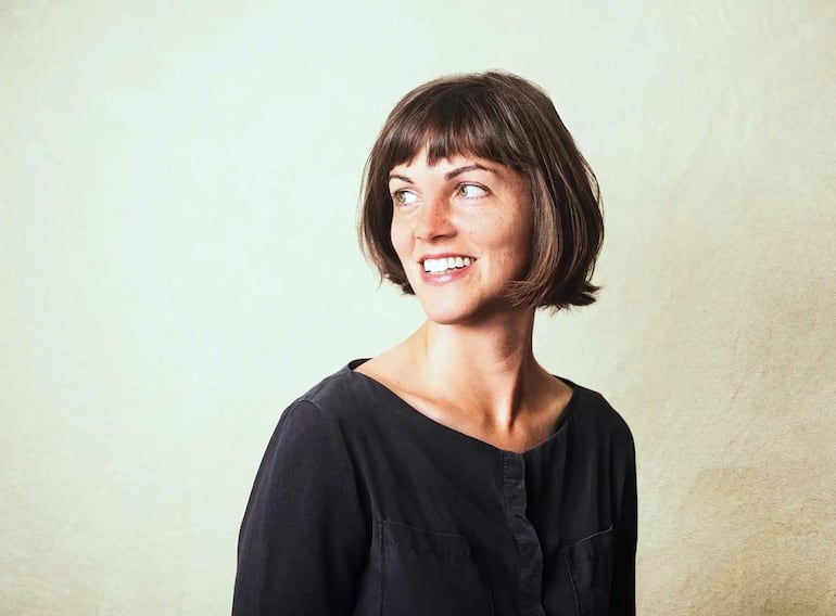 Julie Herndon sonriente, con peinado moderno y vestimenta creativa, mientras actúa en un escenario iluminado.