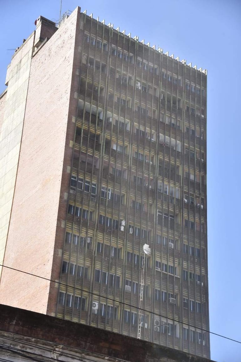Edificio alto de ladrillo con humo denso tras un incendio, en un entorno urbano despejado.
