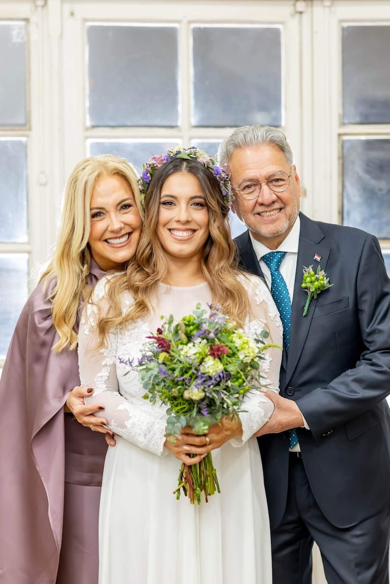 Menchi Barriocanal vestida de novia, abrazada por su madre Menchi Barriocanal en un salón decorado, todos sonrientes y felices.