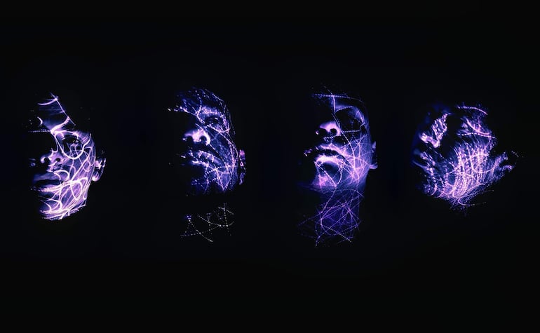 Cuatro rostros indefinidos iluminados por luces púrpuras en un fondo negro, creando una atmósfera dinámica en un estudio.