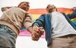 Imagen de referencia: dos personas agarrándose de la mano con una bandera del orgullo LGBTI de fondo.