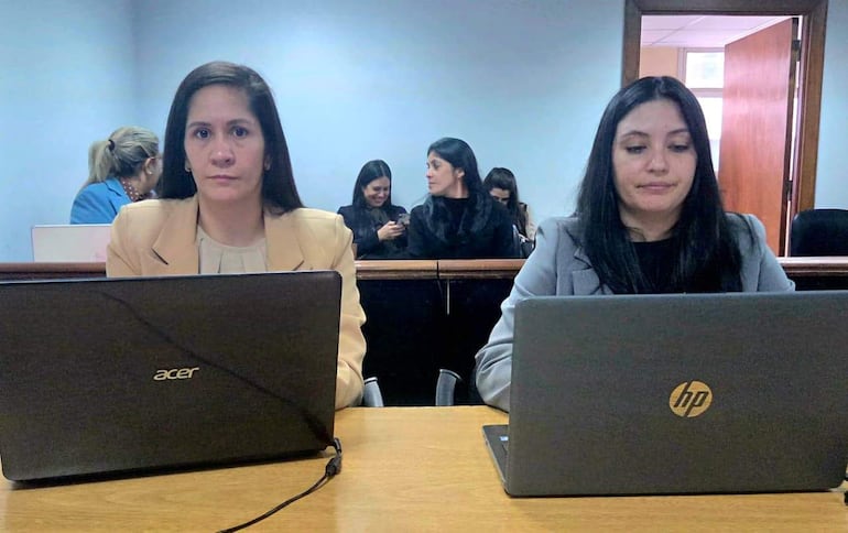 Verónica Valdez en blazer claro y Jimena Ibáñez en blazer gris, ambas serias frente a laptops en oficina con paredes azules.
