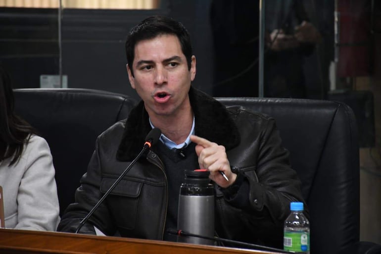 Álvaro Grau habla con fervor, vestido con chaqueta de cuero y camisa azul, mientras una mujer en abrigo claro lo escucha.